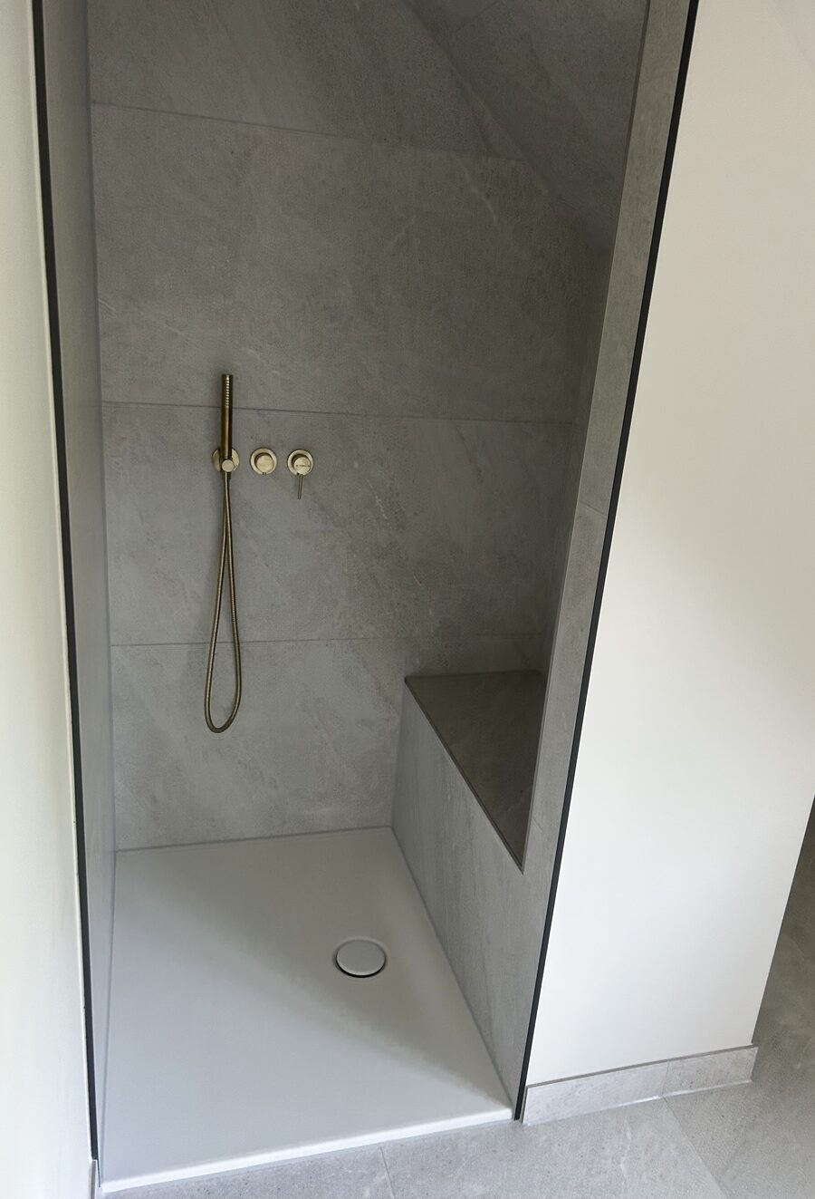 Sanierte Dusche mit Naturstein-Fliesen und goldener Armatur